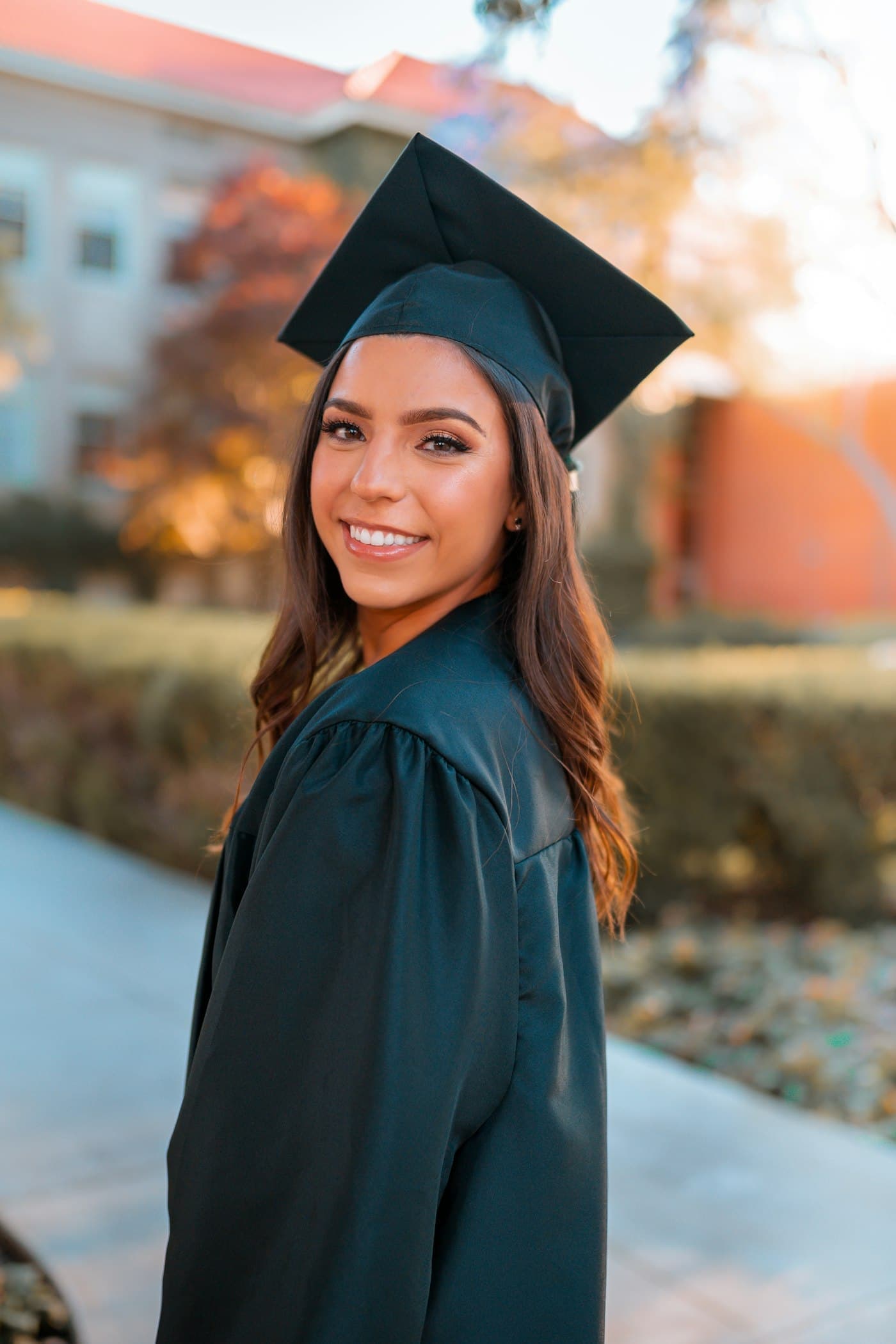 A smiling graduate in cap and gown outside a university building